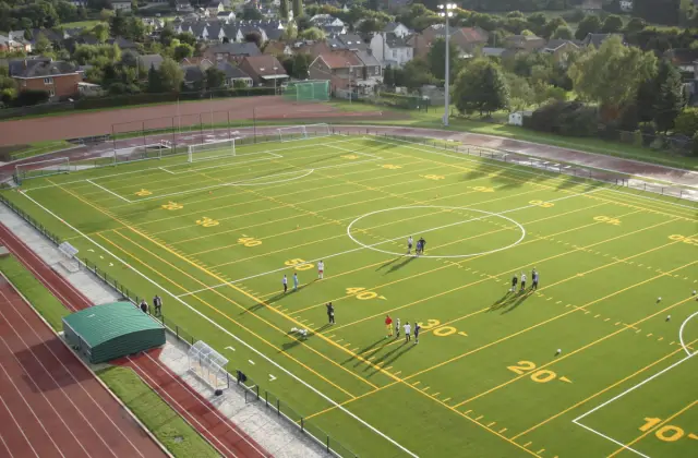 Vista aérea de um campo de relva artificial com linhas de jogo, cercado por uma pista de atletismo